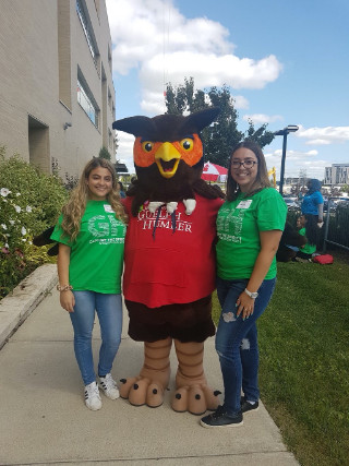 Two students in green orientation shirts posing outside with Swoop mascot